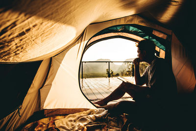 Side view of man sitting in tent during sunset