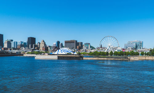 View of ferris wheel by buildings against blue sky