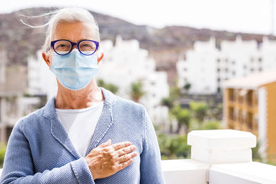 Portrait of senior woman wearing mask gesturing while standing outdoors