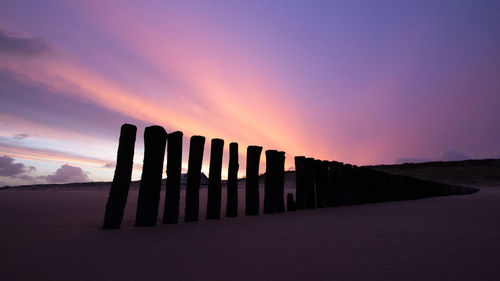 Silhouette wooden posts against dramatic sky during sunset