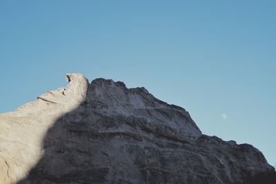 Low angle view of rock formation against clear blue sky with moon