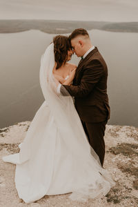 Low angle view of bride and bridegroom standing at beach