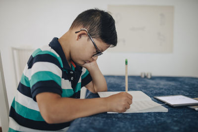 Side view of disabled boy writing on book while sitting at table