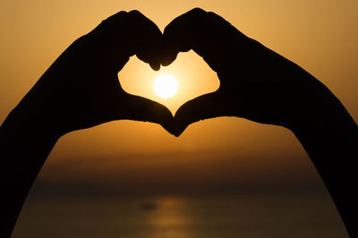 Close-up of hand holding heart shape against sky during sunset