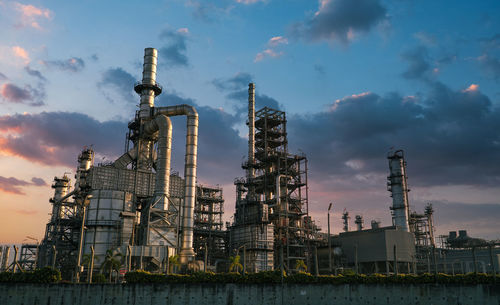 Low angle view of illuminated factory against sky during sunset