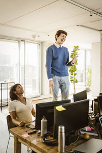 Happy entrepreneur standing on chair by colleague at desk in creative office