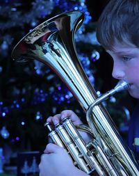 Close-up of boy playing musical instrument against christmas tree at night