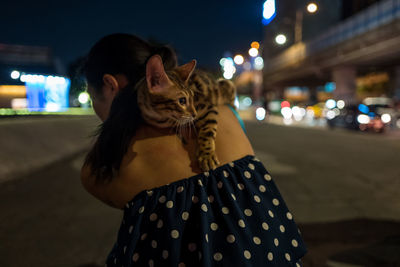 Rear view of woman carrying cat on street in city at night