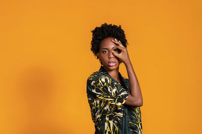 Young african american woman with short hair dressed in a summer shirt posing on an orange colored 