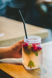 Cropped hand holding drink in mason jar on wooden table