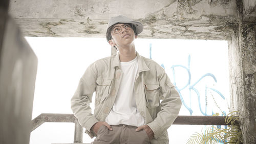 Young man looking away while standing against wall