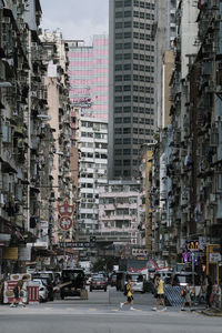 View of people and cars on road by buildings in city