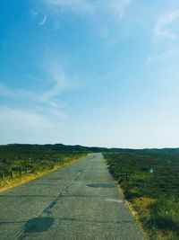 Empty road amidst field against sky