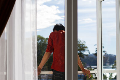 Man standing by window against sky