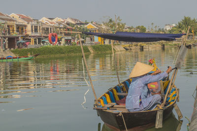 Man sitting on boat in lake against sky