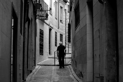 Rear view of man walking in alley amidst buildings