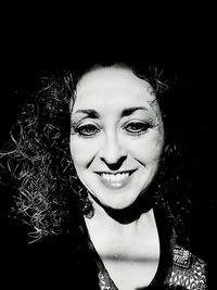 Portrait of smiling young woman against black background