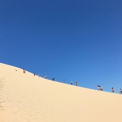 Low angle view of people walking on sand dune against clear sky