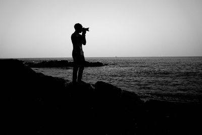 Side view of silhouette man standing at sea against clear sky