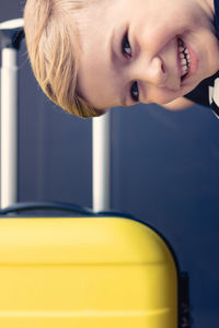 Close-up portrait of smiling boy with yellow luggage