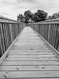 Wooden footbridge on boardwalk against sky