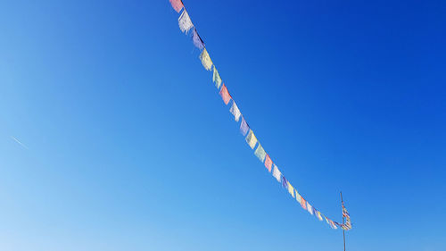 Low angle view of prayer flags hanging against clear blue sky