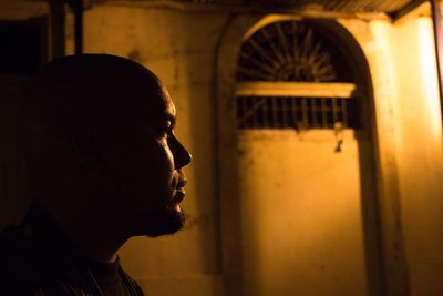 Side view of thoughtful young man against building at night