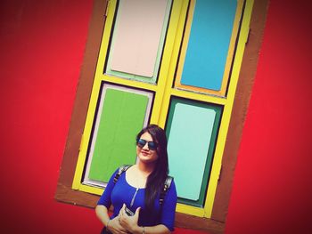 Portrait of smiling young woman standing against wall at home