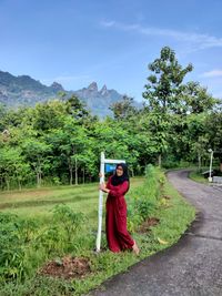 Full length of woman sanding by directional sign against tree