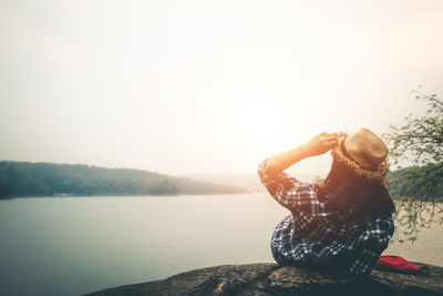 Woman sitting by lake against sky