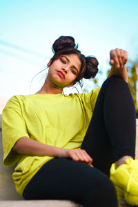 Low angle portrait of young woman sitting against sky