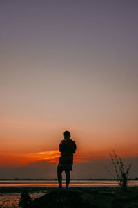 Rear view of silhouette man standing on beach against sky during sunset