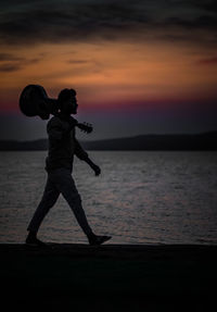 Silhouette man standing on beach against sky during sunset