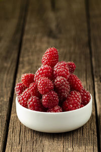 Fresh ripe raspberries in a white ceramic bowl on a dark brown wooden table with space for text