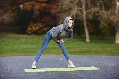 A brunette girl in a tracksuit performs morning sports exercises on yoga mat.