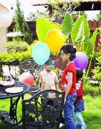 Siblings with colorful helium balloons in yard during birthday