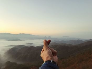 Cropped hand against mountains during sunset