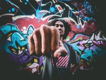 Midsection of man holding multi colored standing against graffiti wall