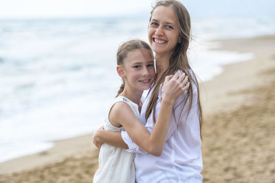Portrait of smiling mother and daughter embracing at beach