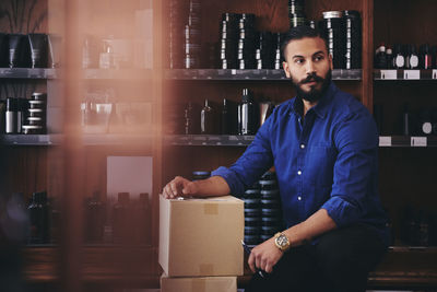 Salesman looking away while kneeling by boxes in deli