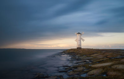 Lighthouse by sea against sky during sunset