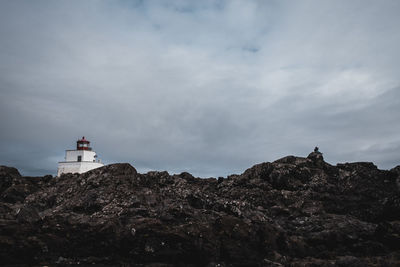 Lighthouse on rock by building against sky