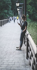 Candid side view young woman standing on the bridge in public park and playing phone, hope and dream