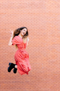 Portrait of young woman jumping against brick wall