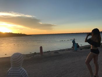 People standing on beach against sky during sunset