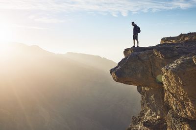 Man standing on rock formation against sky