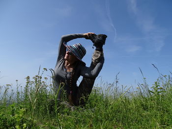 Flexible woman stretching leg on grassy field against sky