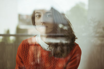 Portrait of serious young woman behind glass pane