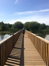 Rear view of man on footbridge over lake against sky