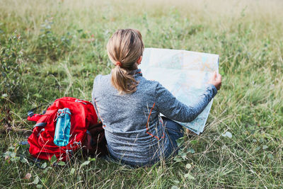 Woman with backpack having break during trip in mountains looking at map sitting on grass